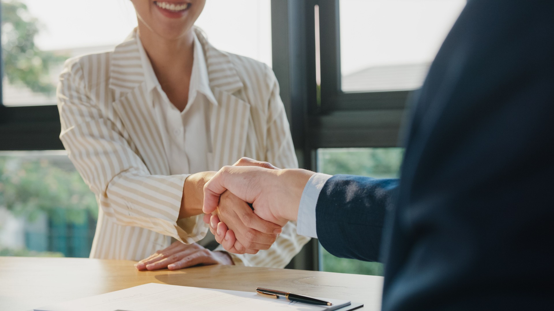Closeup of young Asian businessman sign a contract investment professional document agreement and shake hands at office. Businesspeople in workplace.